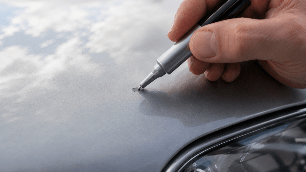 Hand trägt mit Lackstift Farbe auf einen kleinen Steinschlag am Auto auf
