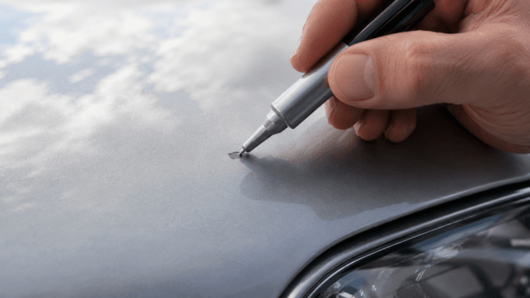 Hand trägt mit Lackstift Farbe auf einen kleinen Steinschlag am Auto auf